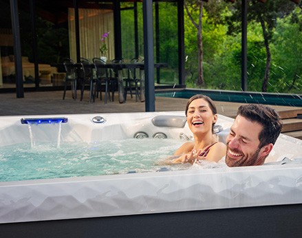 Woman playfully splashing man with water in a hot tub.